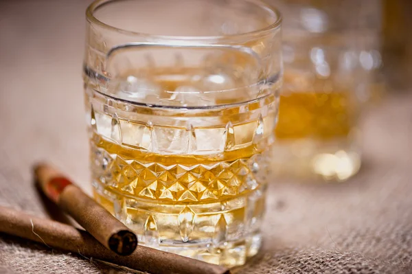 Close-up of whiskey glass on the rocks with cigars and vintage background