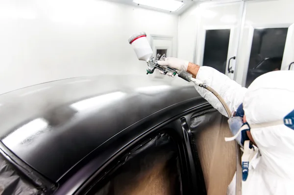 Qualified worker spraying black paint on a car in special painting booth
