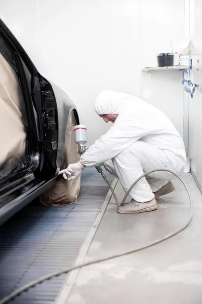 Automotive mechanical engineer painting the body of a black car
