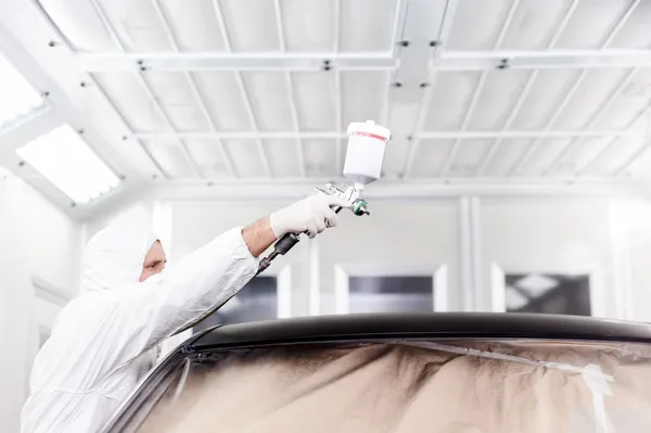 Auto engineer painting a black car in special garage and wearing protective gear