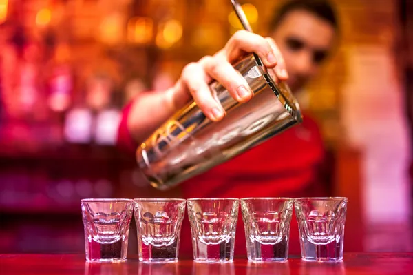 Bartender pouring strong alcoholic drink into shots at nightclub
