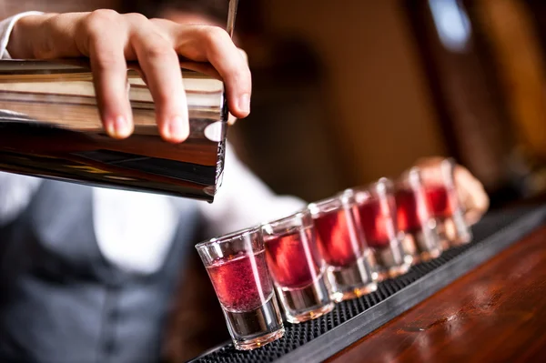Close-up of barman hand pouring alcohol into shot glasses in a nightclub or bar