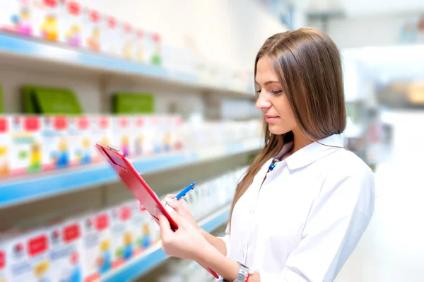 Beautiful blonde pharmacist in drugstore or pharmacy taking notes. Portrait of health care doctor in pharmacy writing on clipboard