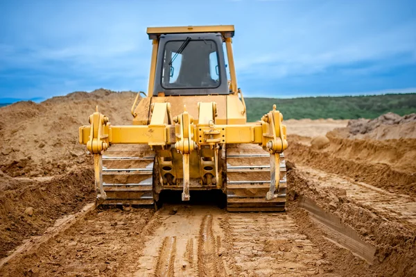 Bulldozer with steel blade moving soil and sand around and working in a sandpit on construction site of a house, road or industrial hall