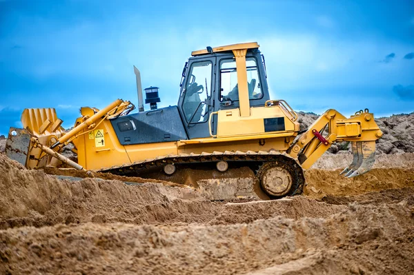 Bulldozer or excavator working with soil on construction site of building, road or industrial hall