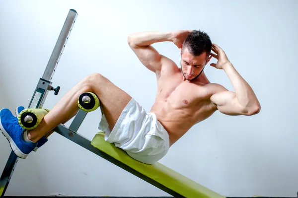 Handsome muscular man doing sit-ups on a incline bench at fitness center or gym