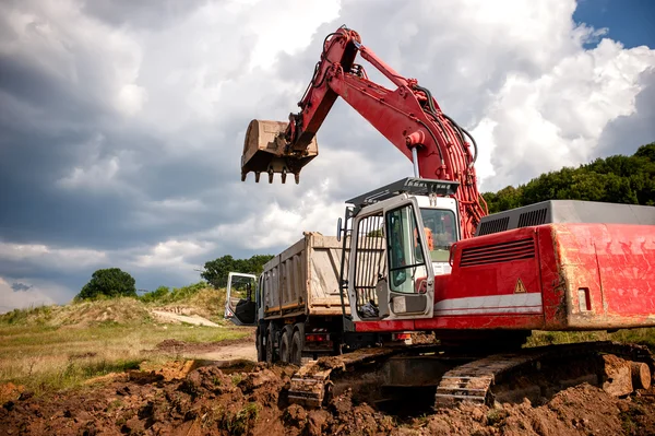 Heavy bulldozer and excavator loading and moving red sand or soil on road construction site or quarry