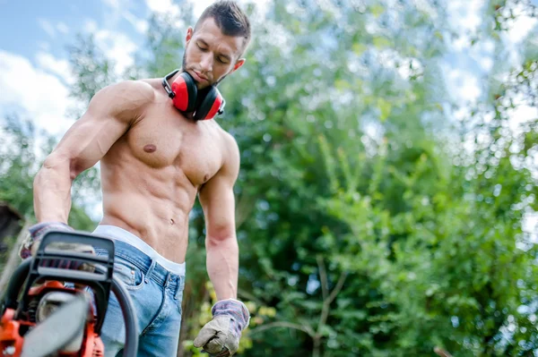 Portrait of aggressive athletic man with chainsaw getting ready for fire wood cutting
