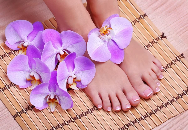 Pedicure with pink orchid flowers on bamboo mat. Beautiful