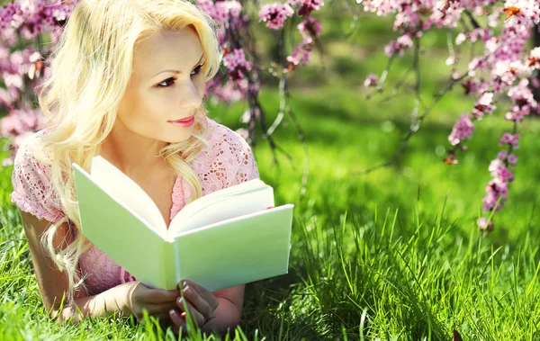 Blonde Woman with Book under Cherry Blossom. Beautiful girl