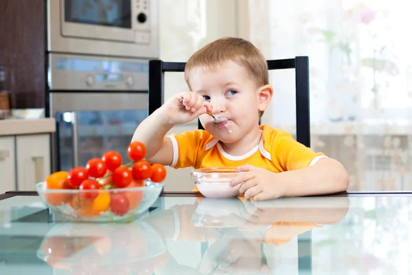 Child boy eating healthy food in kitchen