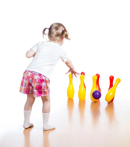 Kid throwing ball to knock down toy bowling pins. Focus on child