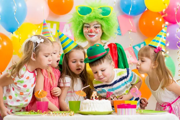 Kids with clown celebrating birthday party and blowing candles o