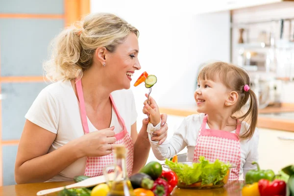 Kid daughter feeding mother vegetables in kitchen