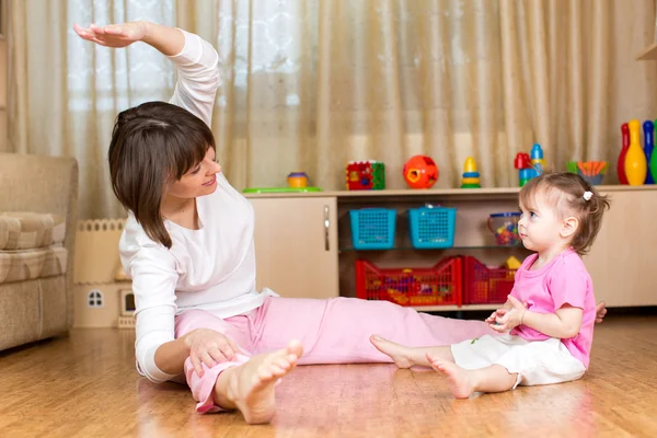 Mom and kid doing exercises sitting on the floor in home interio