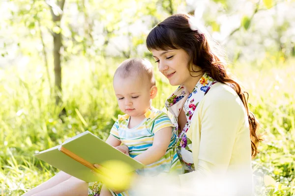 Happy mother reading a book to child outdoors