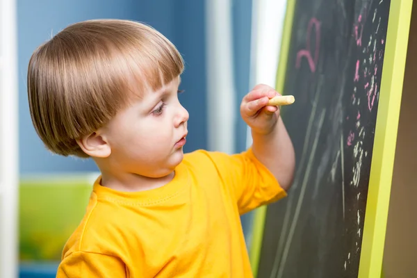 Little boy draws with chalk on blackboard