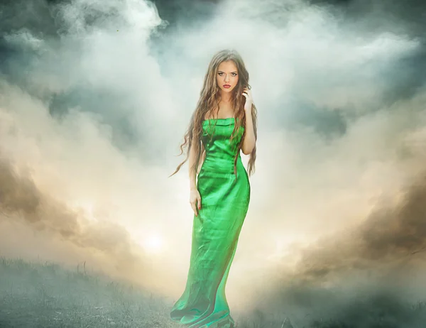 Beautiful girl in green dress standing in fog