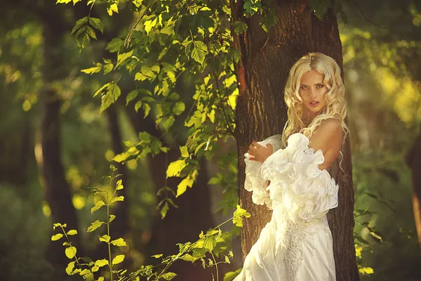 Blonde bride angel in long white skirt standing in forest