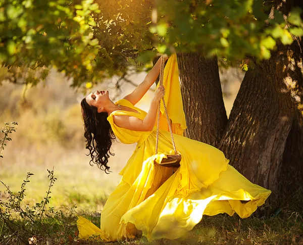 Beautiful girl in a yellow dress riding on a swing