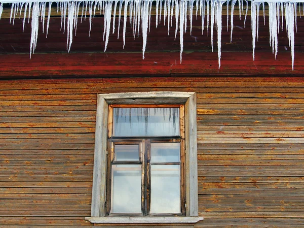 Icicles on the roof of a wooden house with windows