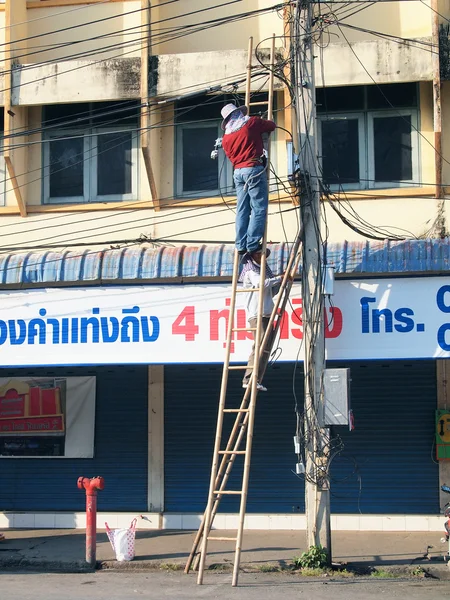 LOP BURI, Thailand - DEMCEMBER 8, 2012: Two Thai electricians are fixing confusing electricity lines on a pole.