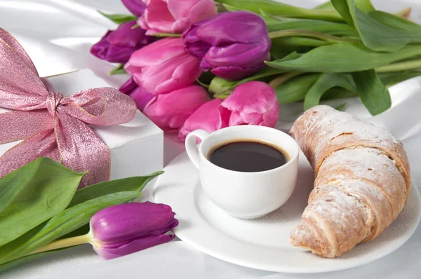 Breakfast with coffee and croissant, gift box and tulips on white silk