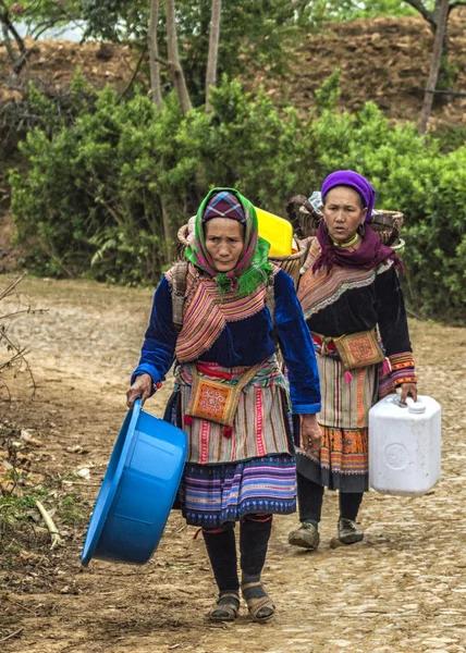 Two Hmong women loaded up baskets on their backs come around the bend in the road.