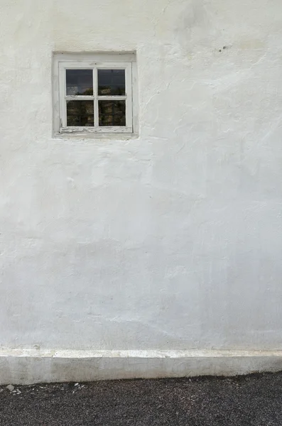 The old white plastered wall with a small window and a gravel pa