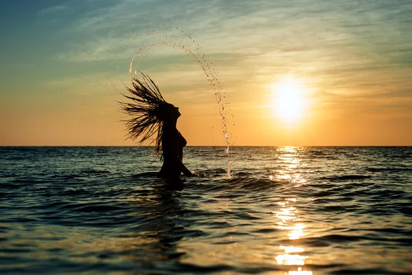 Silhouettes of woman jumping in ocean