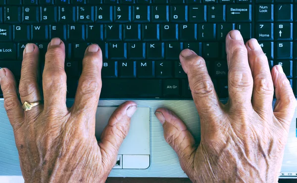 Old hands typing on computer keyboard