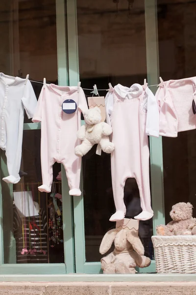 Baby clothing and teddy bear in window