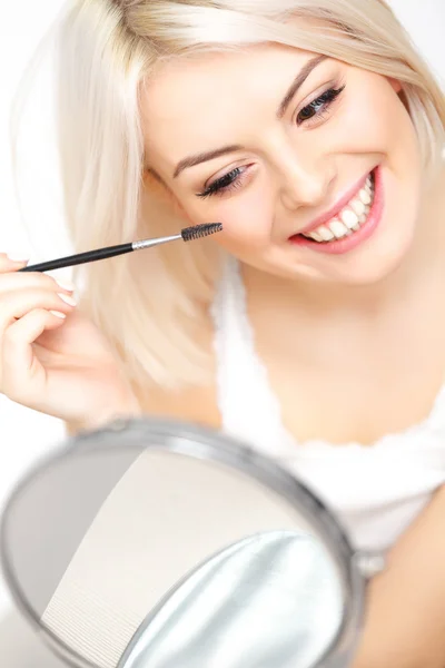 Woman applying mascara on eyelashes.