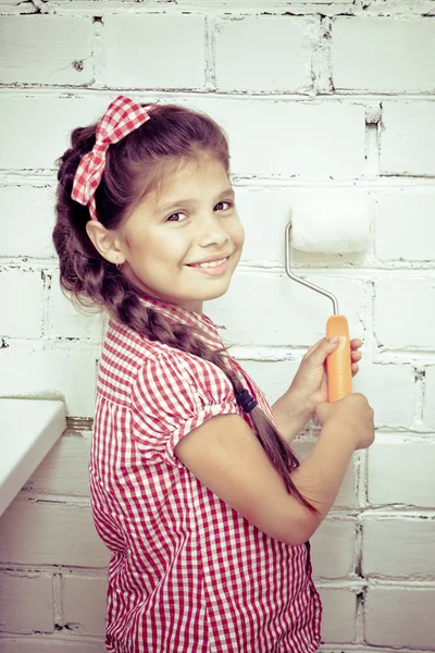 Girl holding paint roller on brick wall