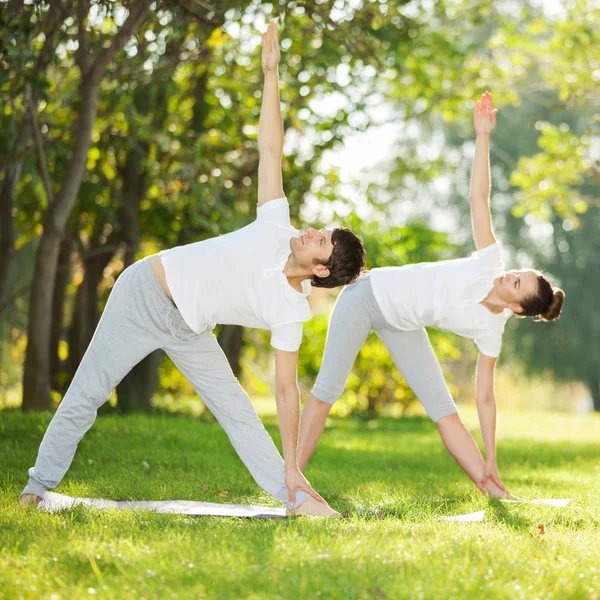 Couple Yoga, man and woman doing yoga exercises in the park