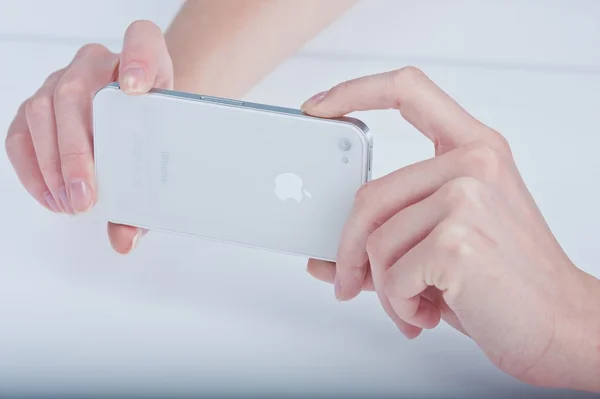 Female hands with a manicure keeps white iphone 4 on a white