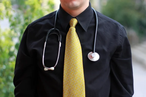 Doctor standing in front of trees with yellow tie and black shirt