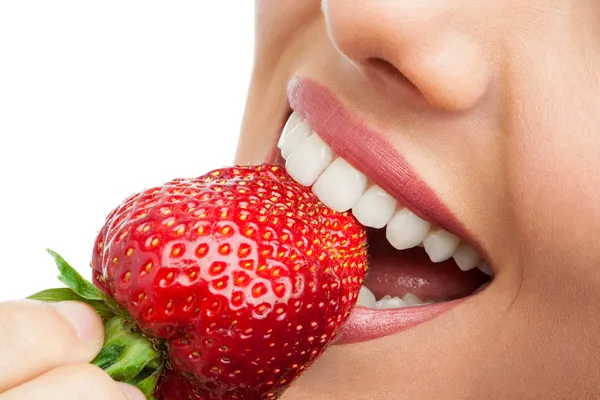 Extreme close up of teeth biting strawberry.