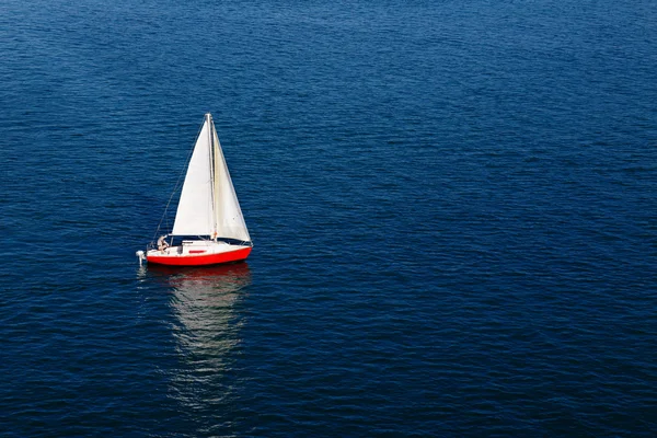 A lone white sail on a calm blue sea