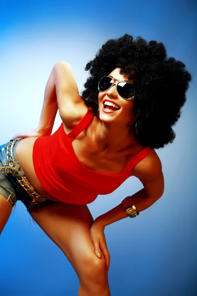 Smiling tanned woman with afro hair posing against blue background