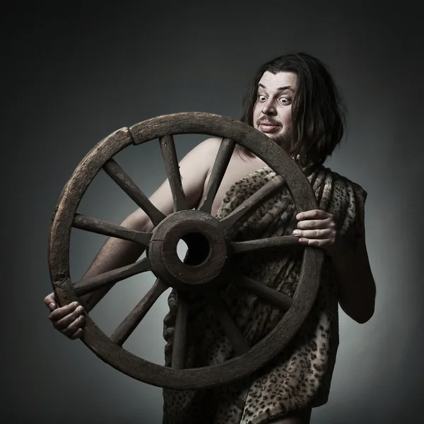 Caveman wearing leopard skin hold old wooden wheel.