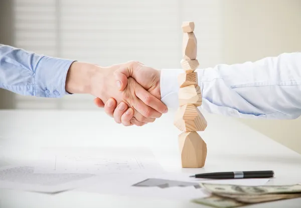 Business people shake hands near built wooden tower