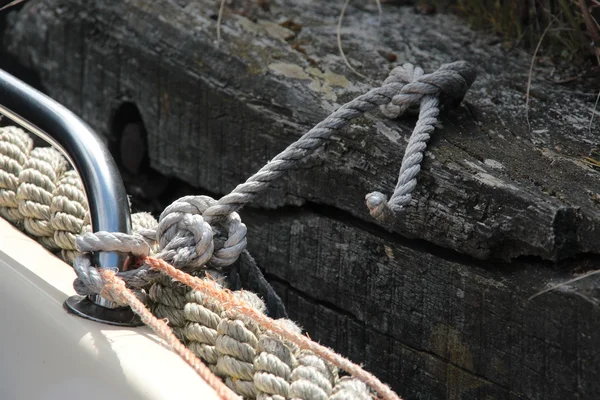 Sailor hawser rope moored to the old worn wooden pier of marina