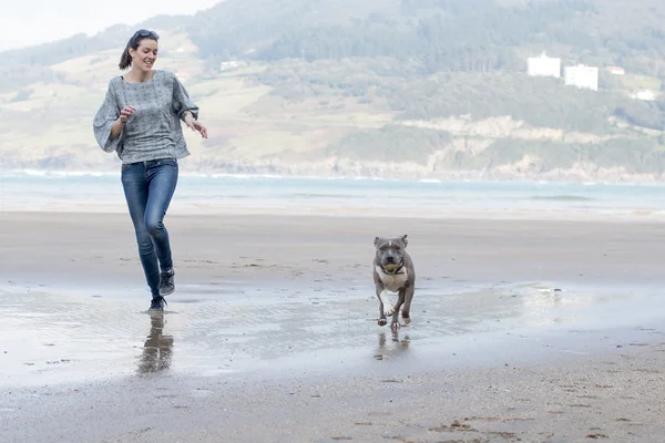 Dog and young woman running and playing in the beach.