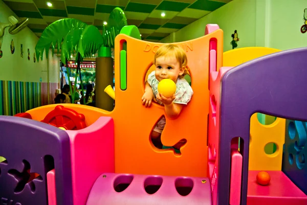 Girl 1,5 years old with yellow ball in hand has fun in game complex