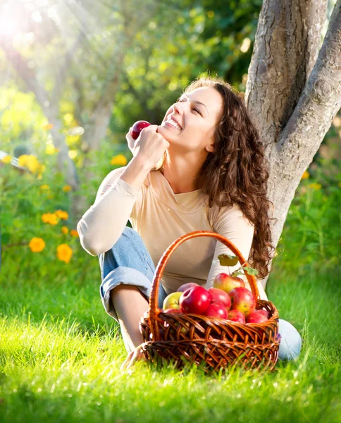 Happy Smiling Young Woman Eating Organic Apple in the Orchard