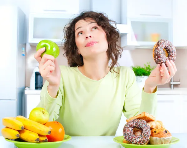 Diet. Beautiful Young Woman choosing between Fruits and Sweets