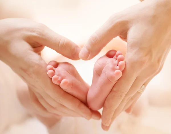Tiny Newborn Baby\'s feet on female Heart Shaped hands closeup