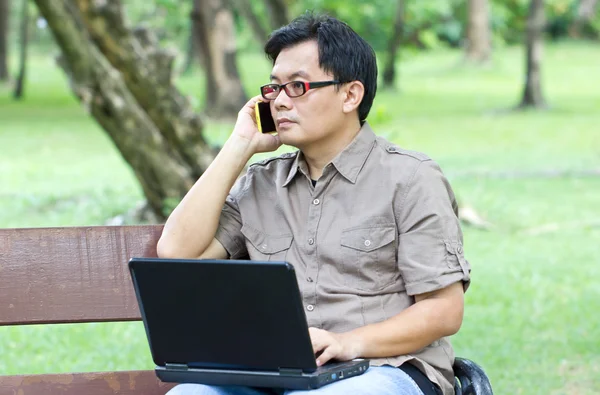 Asian man with mobile phone working with laptop