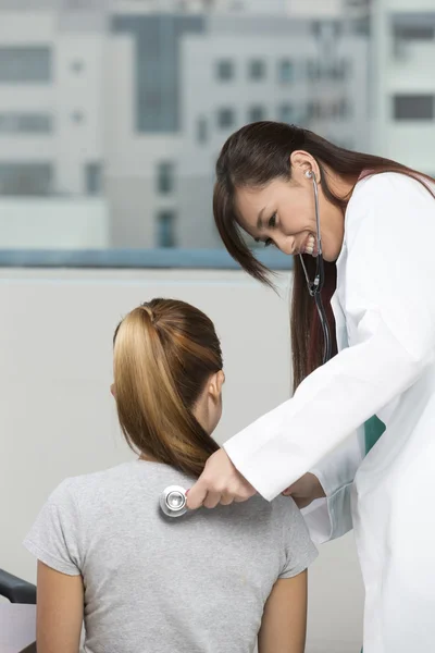 Chinese doctor checking female patient with a stethoscope